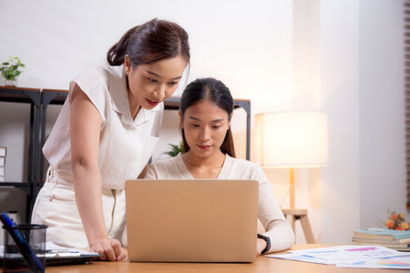 Two young asian businesswoman planning and strategy about marketing and financial with colleagues looking laptop, meeting and working on laptop computer with partner, business and consulting.の写真素材