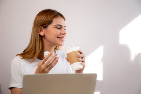 Happiness young caucasian businesswoman drinking coffee while working on laptop computer in home office, happy business woman drinking beverage while using laptop for relax, business concept.の写真素材
