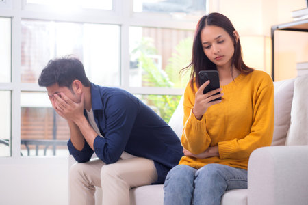 Unhappy asian couple sitting on sofa having relationship problem in living room at home, emotion...