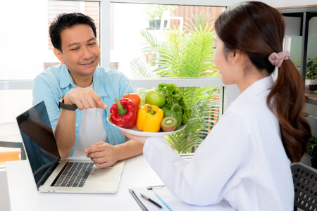 Asian nutritionist holding fresh fruits vegetables during consultation with patient in clinic, wellness and healthy eating, woman dietitian or consultation explaining nutrition for weight loss advice.の写真素材