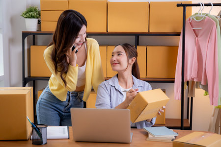 Two asian woman e-commerce startup in home office, two young entrepreneur management order, online seller teamwork, packing product for preparation delivery, retail and shipping, business  concept.の写真素材
