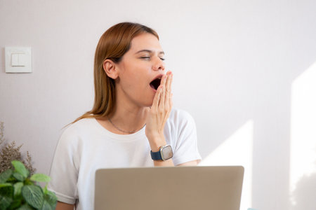 Young caucasian businesswoman working on laptop computer while yawn and tired at home office, business woman using notebook with exhausted and burnout with overworked.の写真素材