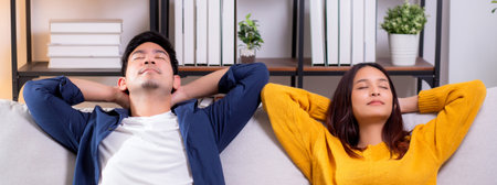 Young asian couple relaxing together on a comfortable sofa at home in the living room, happy and peaceful moment representing love, relationship and modern lifestyle of couple while sitting on couch.の写真素材