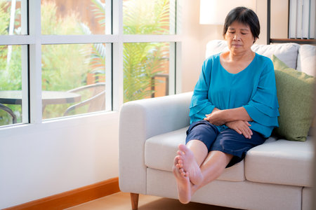 Senior asian woman practice stretch leg for treatment knee pain sitting on sofa in living room at home, physical therapy routine knee and leg strength of elderly, rehabilitation and self care.の写真素材
