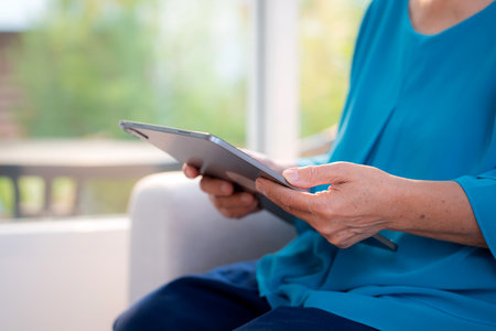 Close up hand senior woman reading tablet in living room at home, online connection and digital...