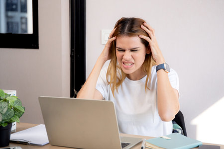 Unhappy young caucasian businesswoman using laptop computer on desk with stress and burnout at home office, business woman working on laptop with frustrated and anxiety, business and expression.の写真素材