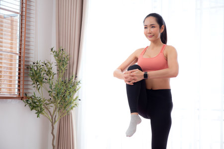 Beautiful young asian woman standing workout with warmup and stretch muscle leg at home, female exercise for relax with sport, motivation and determined for health, one person, sport concept.の写真素材