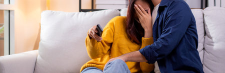 Young asian couple watching a scary or thrilling TV show in living room at home with emotion shock...