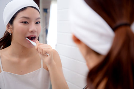 Happy young asian woman brush teeth looking mirror at home, woman clean teeth in bathroom for fresh in morning, hygiene and wellbeing, health and care, wellness and healthcare, self-care.の写真素材