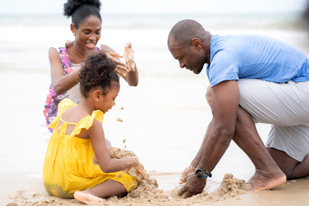 Happy black family sitting playing sand on beach together for leisure during summer vacation, mother and father enjoy bonding with child, recreation holiday, leisure and relaxation on seaside.の写真素材