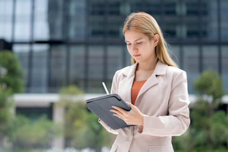 Young caucasian businesswoman writing on digital tablet in city, professional business woman concentrating and note on tablet in business district, employee in modern city, planning marketing.の写真素材