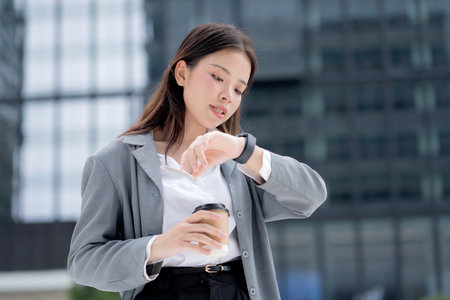 Young asian businesswoman in city talking to smartwatch using voice command with AI, professional business woman using artificial intelligence with watch, virtual assistant.の写真素材