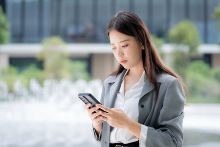 Young asian businesswoman using chatbot or AI message on smartphone outdoors in city, business woman chat on smart phone with AI assistant in urban, artificial intelligence, technology and business.の写真素材