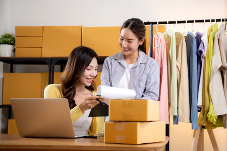 Two asian woman working on laptop and check document while managing and planning online business and checking order, entrepreneur and small business, retail with online seller, startup business.の写真素材
