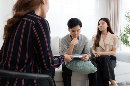 Young asian couple counseling with life insurance with adviser in living room at home, psychologist therapist providing mental health counseling to couple together, planning health insurance.の写真素材