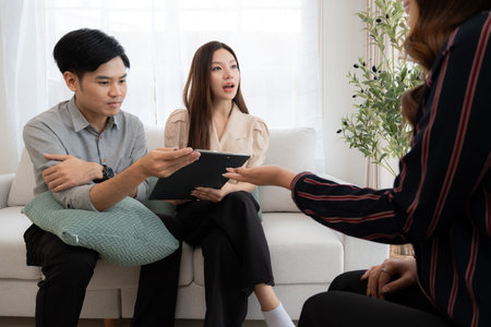 Young asian couple counseling with life insurance with adviser in living room at home, psychologist therapist providing mental health counseling to couple together, planning health insurance.の写真素材