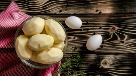 Raw peeled potatoes, two white chicken eggs, allspice on a wooden background with dill branche. Food conceptの写真素材