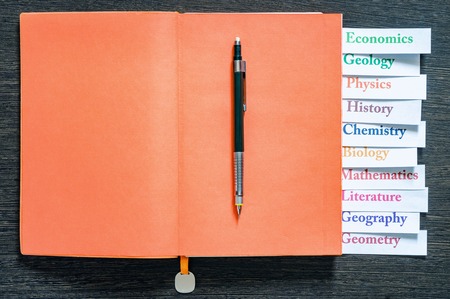 Orange notebook with the name of school subjects. Back to school. Education concept. Top view. Multi-colored letters and numbersの写真素材