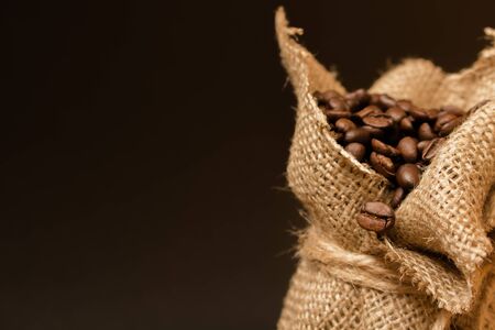 Roasted black coffee beans, spilled from a jute bag into raw planks.
