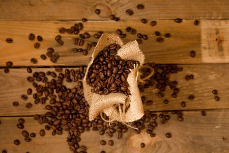 Roasted black coffee beans, spilled from a jute bag into raw planks.