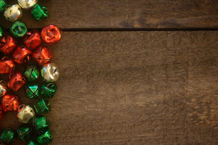 Red, gold, and green Christmas jingle bells on dark wood  line one side of the frame.の写真素材
