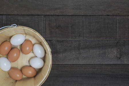 Brown and white chicken eggs in an apple basket on worn dark wood.の写真素材