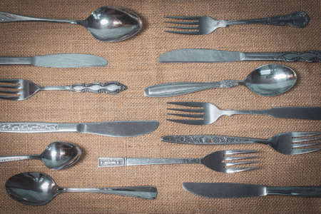 Vintage silverware, including forks, knives, and spoons on burlap table cloth.