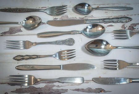 A collection of vintage silverware, including spoons, knives, and forks  on old, worn, white painted...