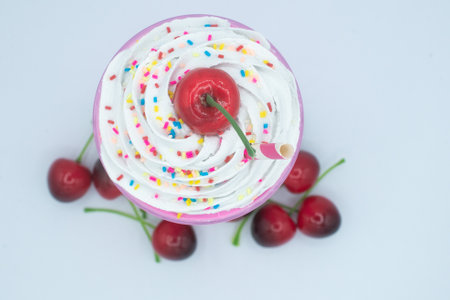 Strawberry milkshake from above with whip cream, rainbow sprinkles, a cherry, and extra cherries around the bottom.の写真素材