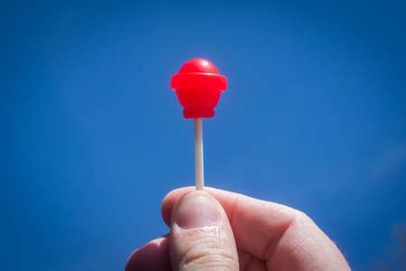 Bright red lollipop held in hand against bright blue sky.の写真素材