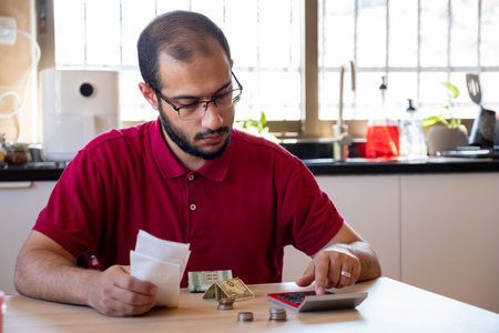 man sitting in the kitchen and calculating the costs of living feeling frustratedの写真素材