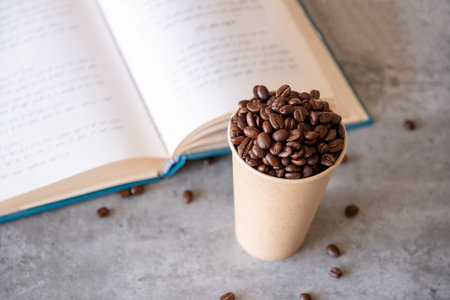 paper cup of coffee full of coffee beans  with grey background and bookの写真素材