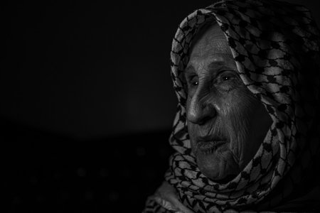 portrait of an old lady in dark background wearing white palestinian keffiyeh with smile on her face looking for freedom and hope to Right of Return for Palestiniansの写真素材