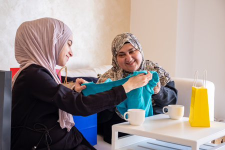 Arabic woman gifting her mother and showing the new clothes after shopping with shopping bags in the background in living roomの写真素材
