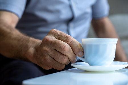 Old man hands holding cup of coffee on white table whearing shirtsの写真素材