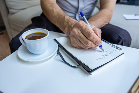 Old man hands writting notes while drinking coffee in living roomの写真素材
