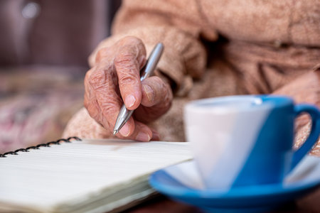 wrinkled hands for elderly person writing notes on his note book while drinking coffeeの写真素材