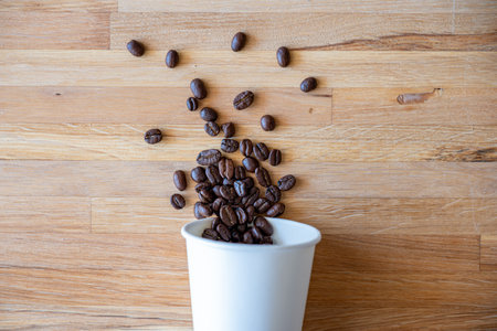 Coffee beans in a white cup on wooden background, top view