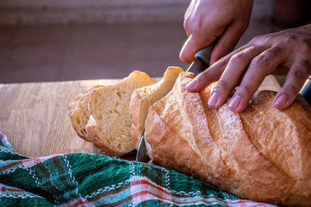 hands holding the knife and cutting the bread into slices to be servedの写真素材