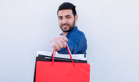 Young male holding shopping bags on white isolated background for black and white friday promotions with cheerful faceの写真素材