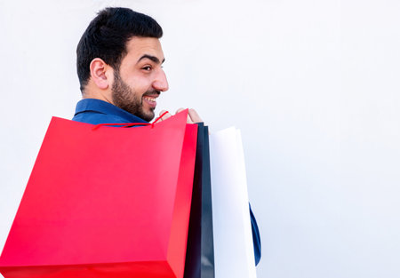 Young male holding shopping bags on white isolated background for black and white friday promotions with cheerful faceの写真素材