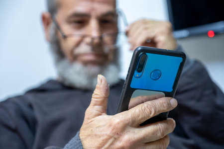 old man holding phone while focusing due to poor eye visionの写真素材