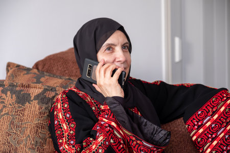 Female wearing palestinian traditional clothes indoor making phone call on couch  with her relatives in palestineの写真素材