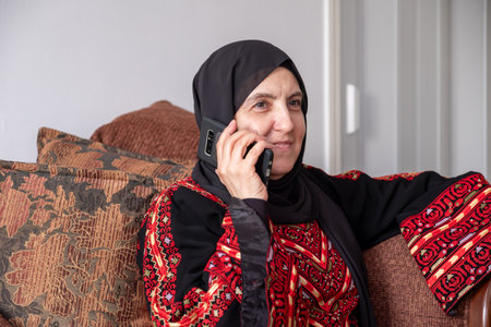 Female wearing palestinian traditional clothes indoor making phone call on couch  with her relatives in palestineの写真素材