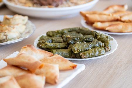 Dish of grape rolls on wooden table from top view with sambousek and qatayef