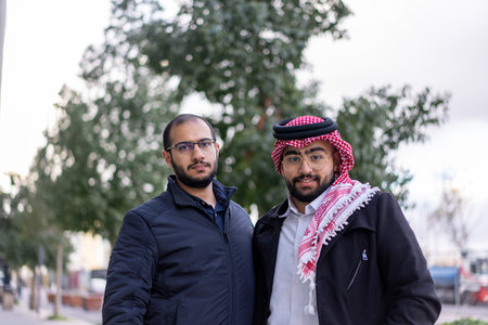 In the backdrop of a sleek, modern urban landscape, two young Arabic businessmen stand confidently.の写真素材