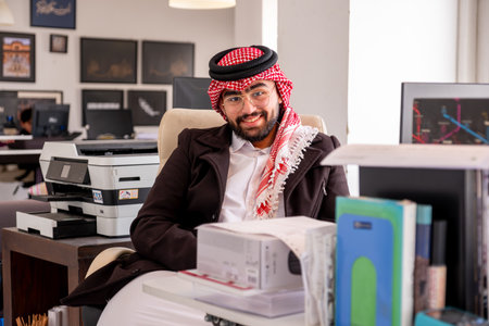 In an elegant office setting, an Arabic gentleman sits comfortably in his chair, exuding confidence and warmth. With a genuine smile gracing his face, he radiates positivity and professionalismの写真素材
