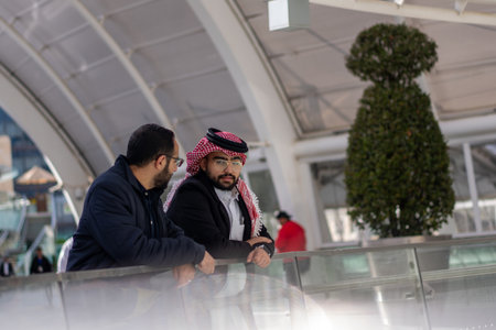 Two arabic males are talking to each other in modern place outdoors like mall shop and huge playing...