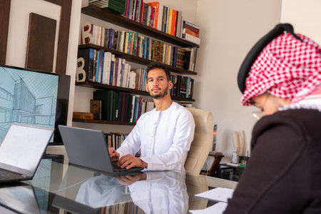 confident arabic male working on his laptop  with modern background  and libraryの写真素材