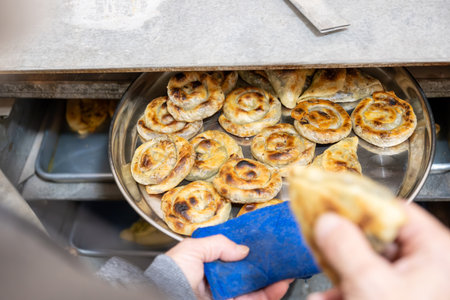 Old man hands holding aluminum plate full of white cheese stuffed pastries and putting it in old ovenの写真素材